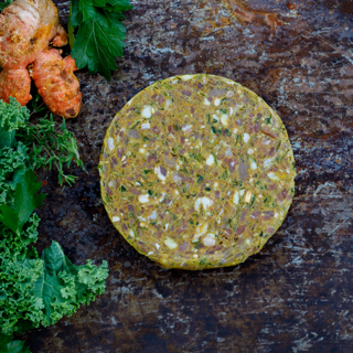 Disk of raw Organic Beef &amp; Tumeric blend dog food on bench with greens and tumeric.